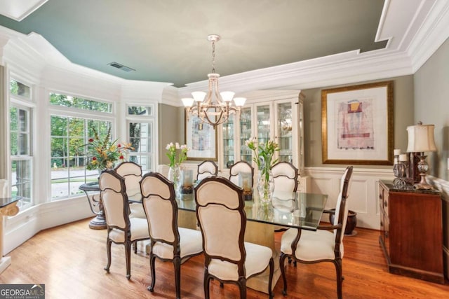 dining room with ornamental molding, light wood-type flooring, and an inviting chandelier