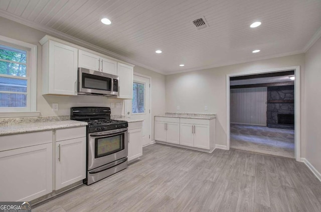 kitchen with crown molding, a stone fireplace, stainless steel appliances, white cabinets, and light hardwood / wood-style flooring