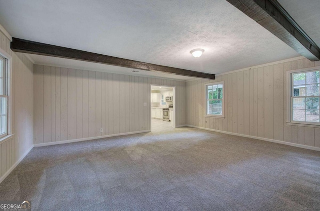 unfurnished room with a wealth of natural light, light colored carpet, and beam ceiling