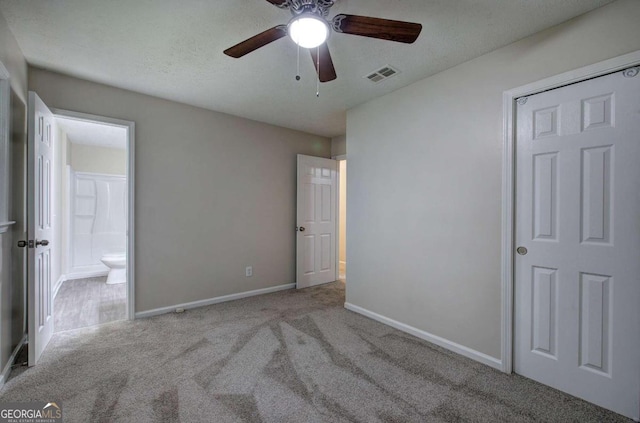 unfurnished bedroom with ceiling fan, a textured ceiling, light carpet, and connected bathroom