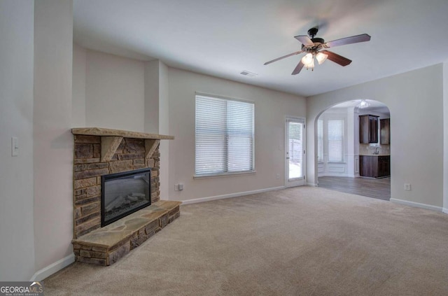 unfurnished living room featuring a stone fireplace, light colored carpet, and ceiling fan