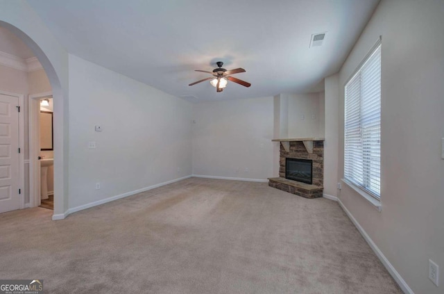 unfurnished living room featuring ceiling fan, light colored carpet, and a stone fireplace