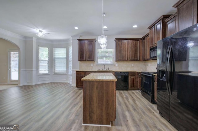 kitchen with a wealth of natural light, light hardwood / wood-style floors, black appliances, and a kitchen island