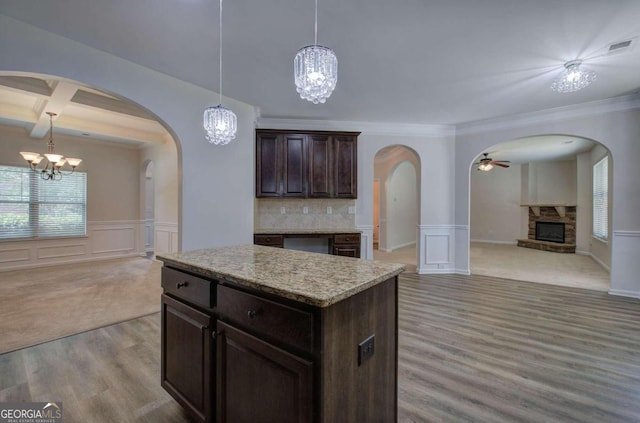 kitchen featuring beamed ceiling, a fireplace, crown molding, a kitchen island, and pendant lighting