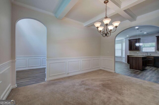 unfurnished dining area with beamed ceiling, dark colored carpet, and ornamental molding