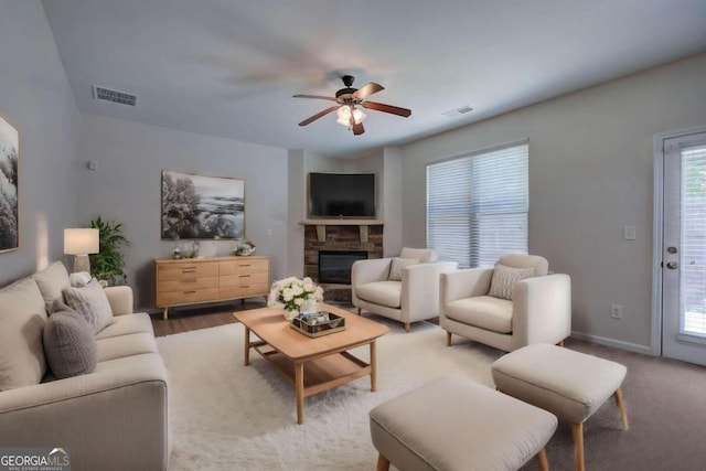 living room with a stone fireplace, wood-type flooring, and ceiling fan