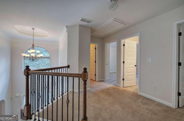 hallway with a tray ceiling, an inviting chandelier, light colored carpet, and crown molding