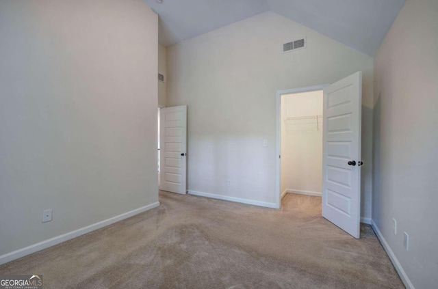 unfurnished bedroom featuring high vaulted ceiling, a closet, a walk in closet, and light colored carpet