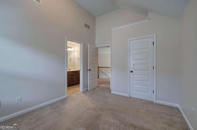 unfurnished bedroom featuring high vaulted ceiling, a closet, light carpet, and ensuite bath