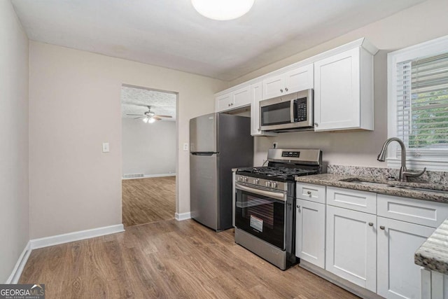 kitchen featuring light stone counters, stainless steel appliances, sink, white cabinets, and light hardwood / wood-style flooring