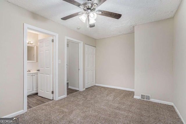 unfurnished bedroom with ceiling fan, connected bathroom, a textured ceiling, and dark colored carpet