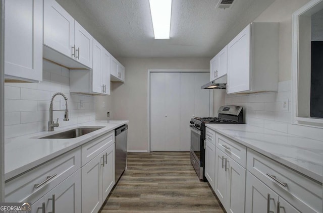 kitchen with wood-type flooring, white cabinets, sink, backsplash, and appliances with stainless steel finishes