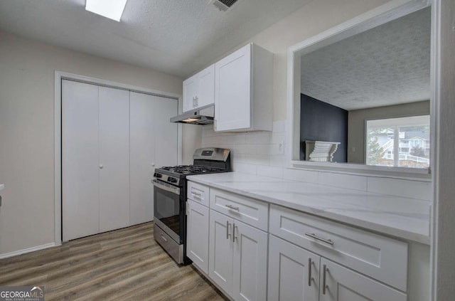 kitchen featuring white cabinets, a textured ceiling, light hardwood / wood-style flooring, and gas stove