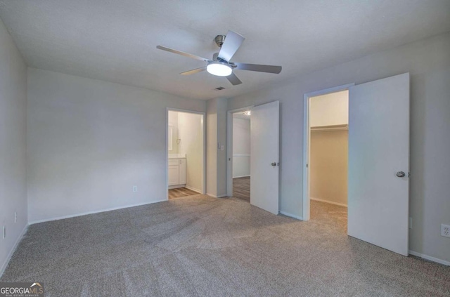 unfurnished bedroom featuring a closet, a spacious closet, ensuite bath, light colored carpet, and ceiling fan