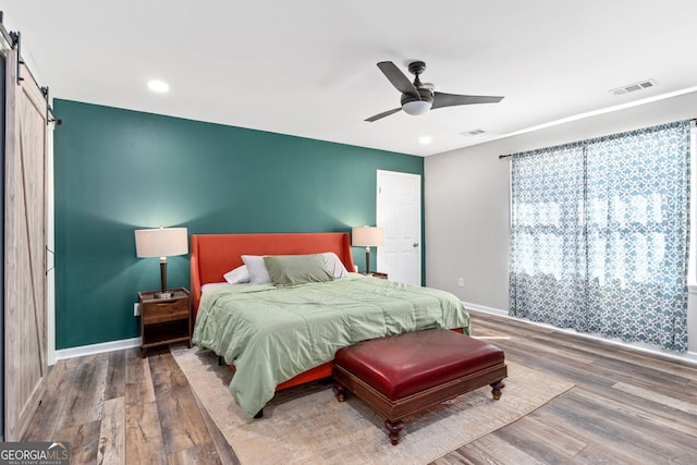 bedroom with a barn door, hardwood / wood-style flooring, and ceiling fan