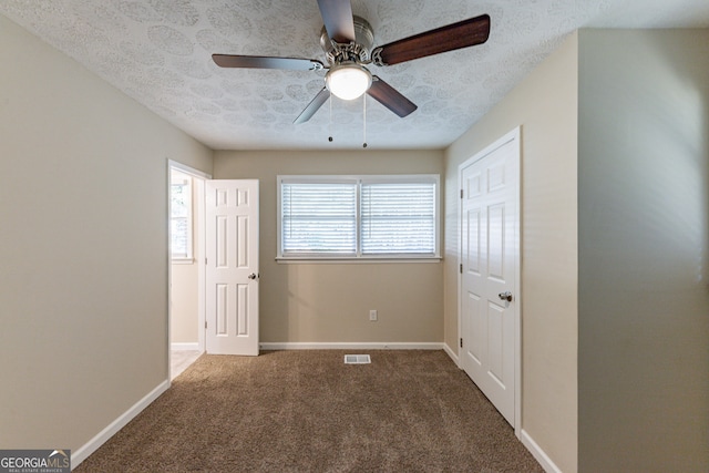 unfurnished bedroom with ceiling fan, dark colored carpet, and a textured ceiling