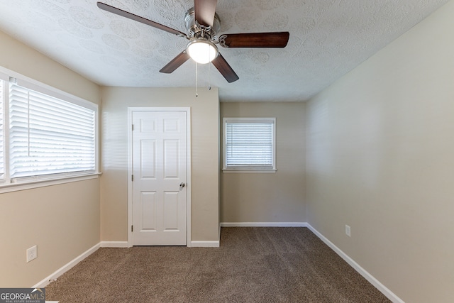 unfurnished bedroom with a textured ceiling, dark colored carpet, and ceiling fan