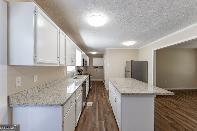 kitchen with white cabinetry, light stone counters, appliances with stainless steel finishes, ornamental molding, and dark wood-type flooring