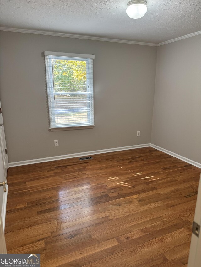 empty room featuring dark wood-type flooring, ornamental molding, and a textured ceiling