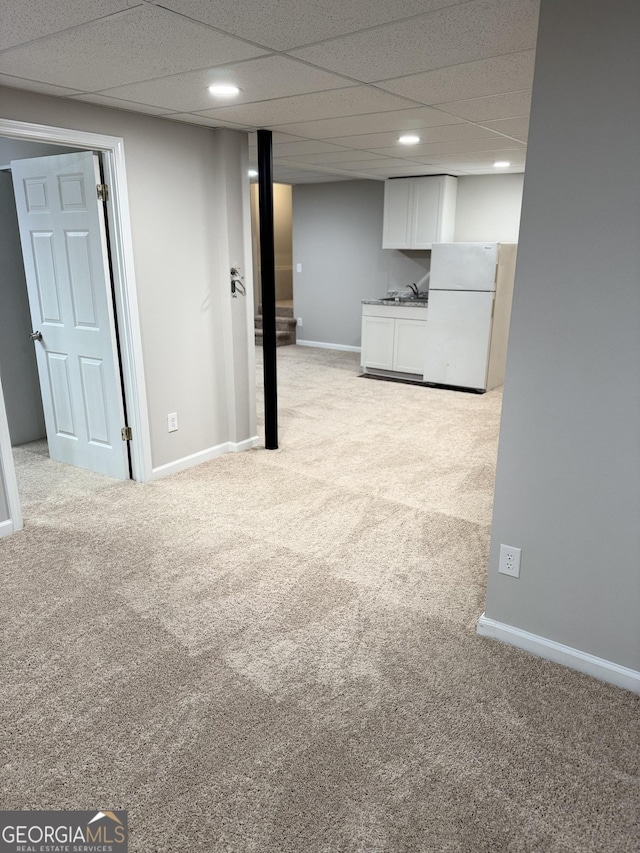 basement featuring light carpet, a drop ceiling, and white fridge