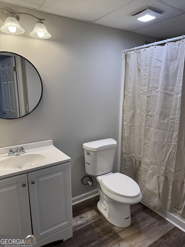 bathroom with wood-type flooring, toilet, a drop ceiling, and vanity