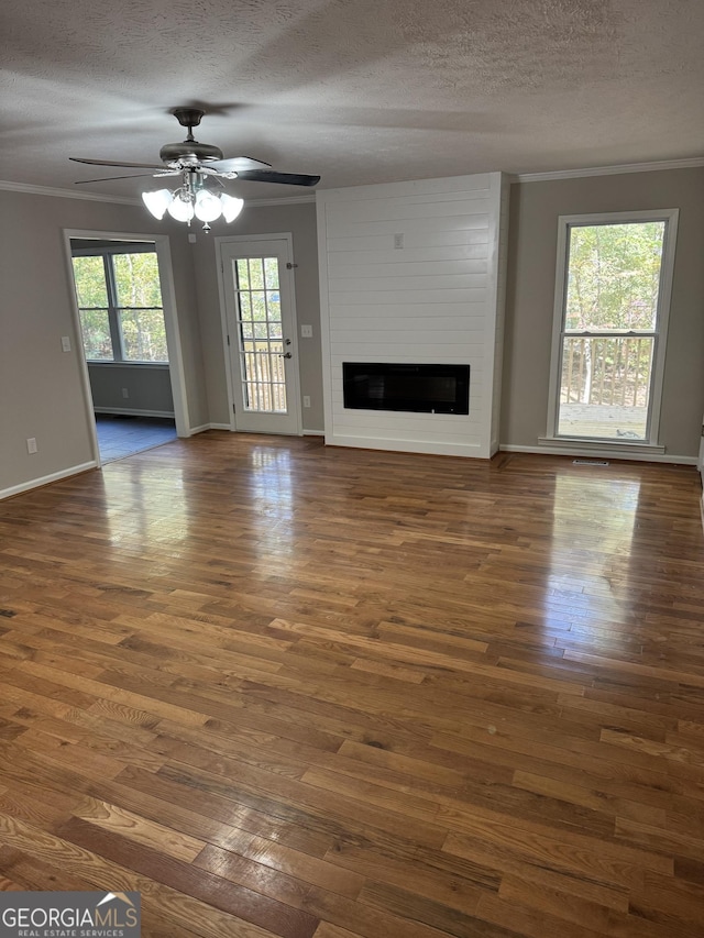 unfurnished living room featuring ceiling fan, ornamental molding, a large fireplace, a textured ceiling, and dark hardwood / wood-style flooring