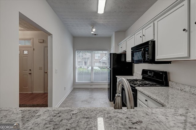 kitchen with light stone counters, black appliances, a textured ceiling, white cabinetry, and light wood-type flooring