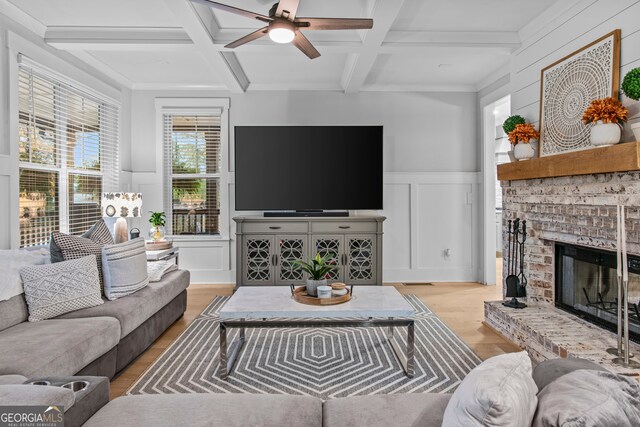 living room featuring beam ceiling, ceiling fan, coffered ceiling, light hardwood / wood-style flooring, and a fireplace