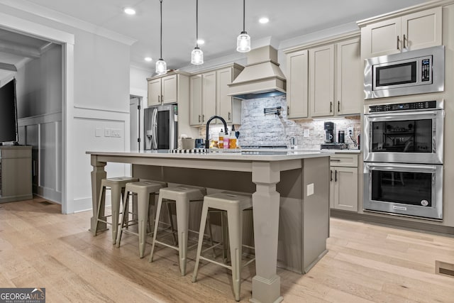 kitchen featuring light hardwood / wood-style flooring, stainless steel appliances, premium range hood, and an island with sink