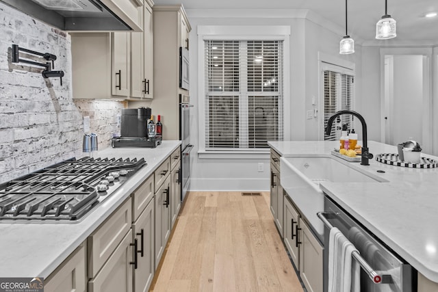 kitchen with appliances with stainless steel finishes, custom exhaust hood, sink, decorative light fixtures, and light hardwood / wood-style floors