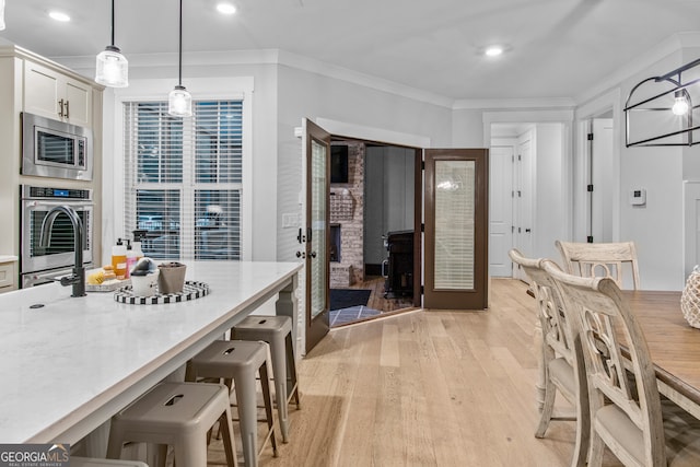 kitchen featuring appliances with stainless steel finishes, ornamental molding, light hardwood / wood-style floors, white cabinetry, and hanging light fixtures