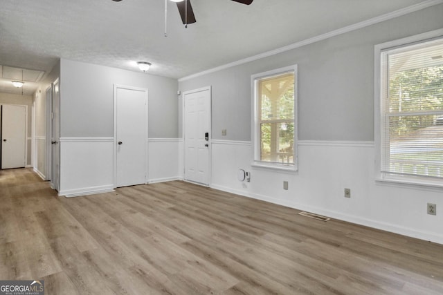 empty room with light wood-type flooring, a textured ceiling, ceiling fan, and ornamental molding