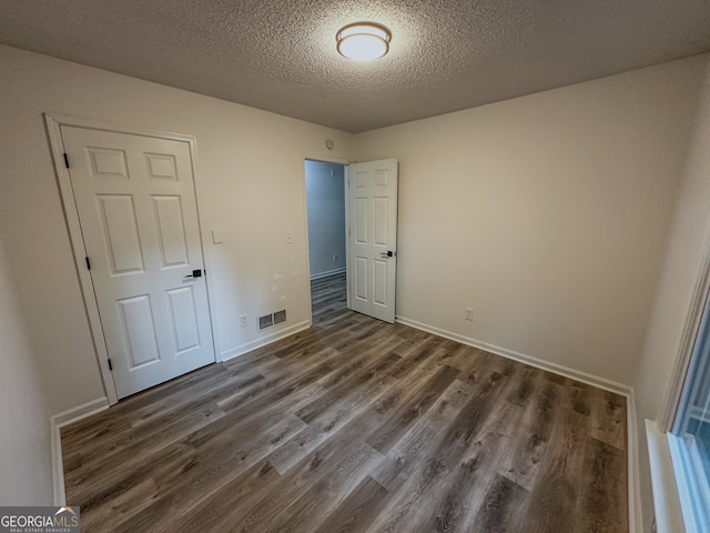 unfurnished bedroom with dark hardwood / wood-style flooring, a textured ceiling, and a closet