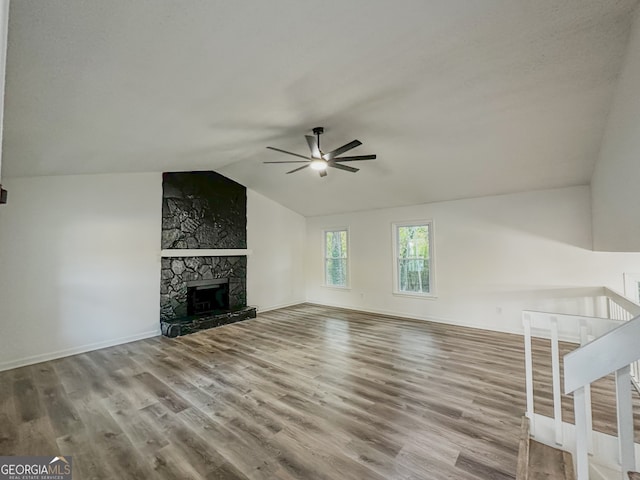 unfurnished living room featuring a stone fireplace, ceiling fan, light hardwood / wood-style floors, and vaulted ceiling