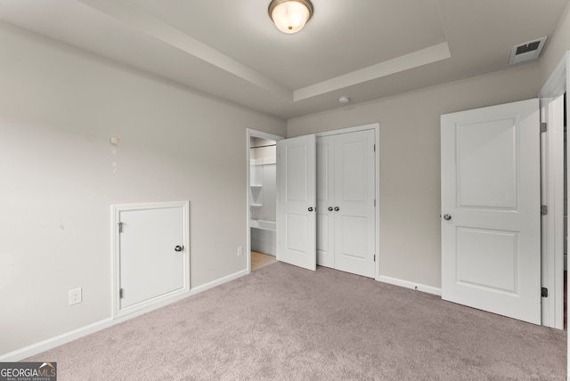 unfurnished bedroom with carpet flooring, ensuite bathroom, a closet, and a tray ceiling