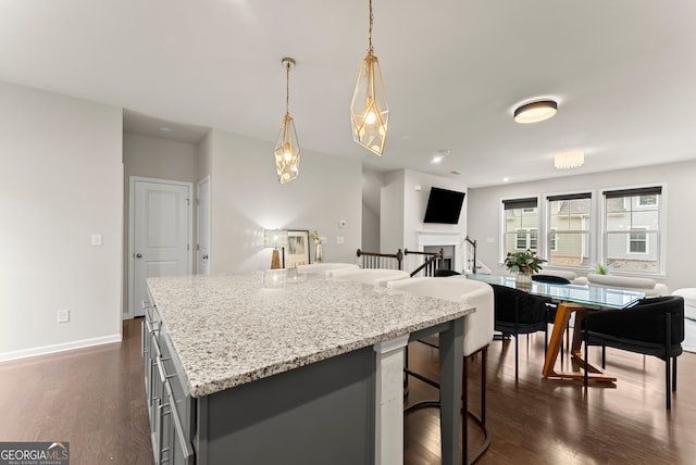 kitchen with light stone countertops, a kitchen breakfast bar, a center island, dark hardwood / wood-style floors, and hanging light fixtures