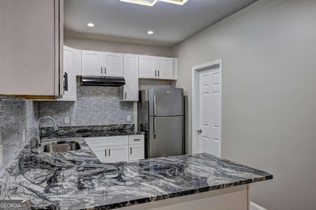 kitchen with dark stone counters, decorative backsplash, sink, white cabinetry, and stainless steel fridge