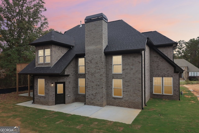 back house at dusk featuring a yard and a patio area