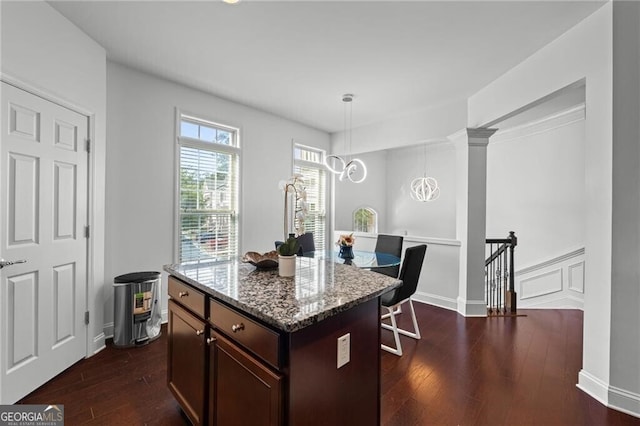 kitchen with dark hardwood / wood-style flooring, light stone countertops, decorative light fixtures, and a center island