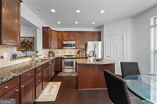 kitchen with light stone counters, appliances with stainless steel finishes, dark hardwood / wood-style floors, sink, and a center island