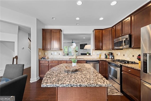 kitchen featuring stainless steel appliances, light stone countertops, dark hardwood / wood-style floors, a kitchen island, and decorative backsplash