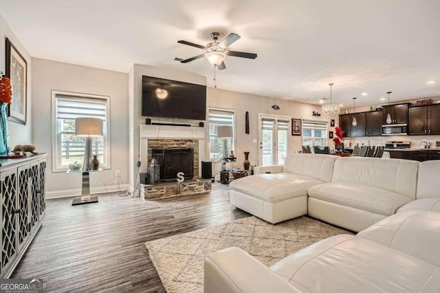 living room featuring light wood-type flooring, a wealth of natural light, a fireplace, and ceiling fan with notable chandelier