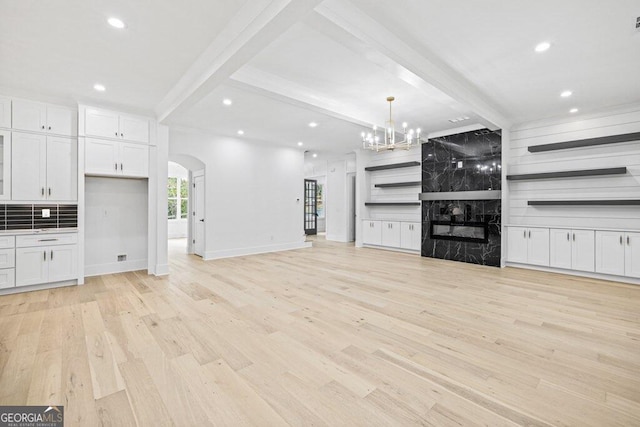 unfurnished living room with beamed ceiling, an inviting chandelier, and light hardwood / wood-style flooring