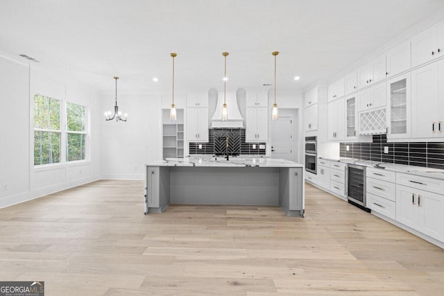 kitchen featuring a large island, pendant lighting, white cabinets, and beverage cooler