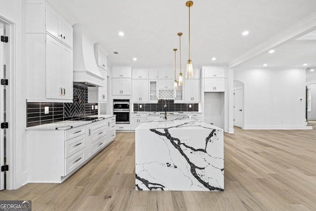 kitchen featuring a large island, light hardwood / wood-style floors, tasteful backsplash, and premium range hood