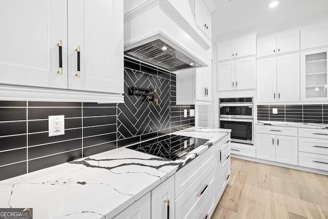 kitchen featuring black cooktop, custom exhaust hood, light stone counters, and white cabinets