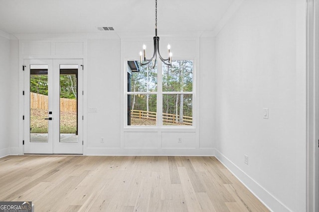 unfurnished dining area featuring ornamental molding, french doors, a notable chandelier, and light hardwood / wood-style floors