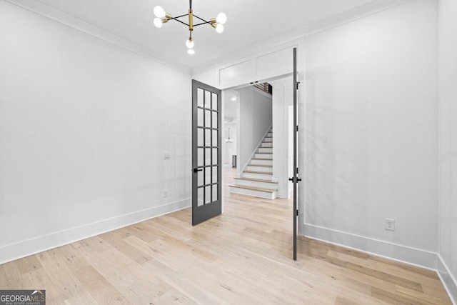 empty room with a chandelier, light wood-type flooring, and crown molding