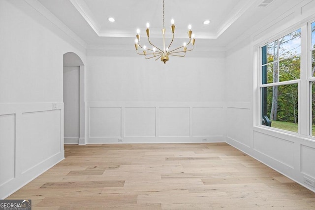 unfurnished dining area with a tray ceiling, an inviting chandelier, ornamental molding, and light hardwood / wood-style flooring