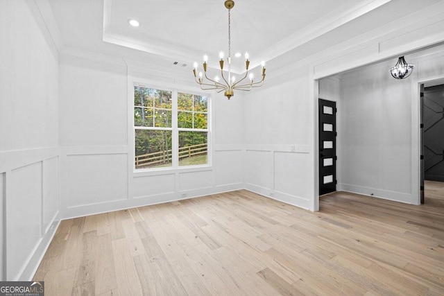 unfurnished room with a notable chandelier, light wood-type flooring, a raised ceiling, and ornamental molding